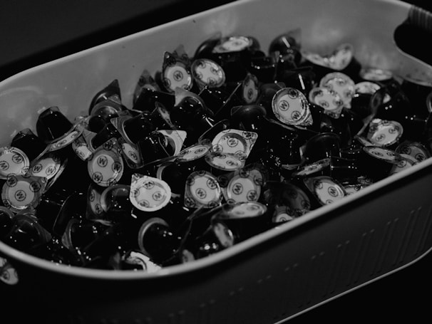 A collection of small cream or sauce cups with lids, arranged closely together in a large rectangular container. The cups appear to have a design on top, likely a logo or brand symbol.