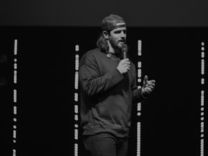 A person speaking into a microphone with a glowing digital interface in the background.