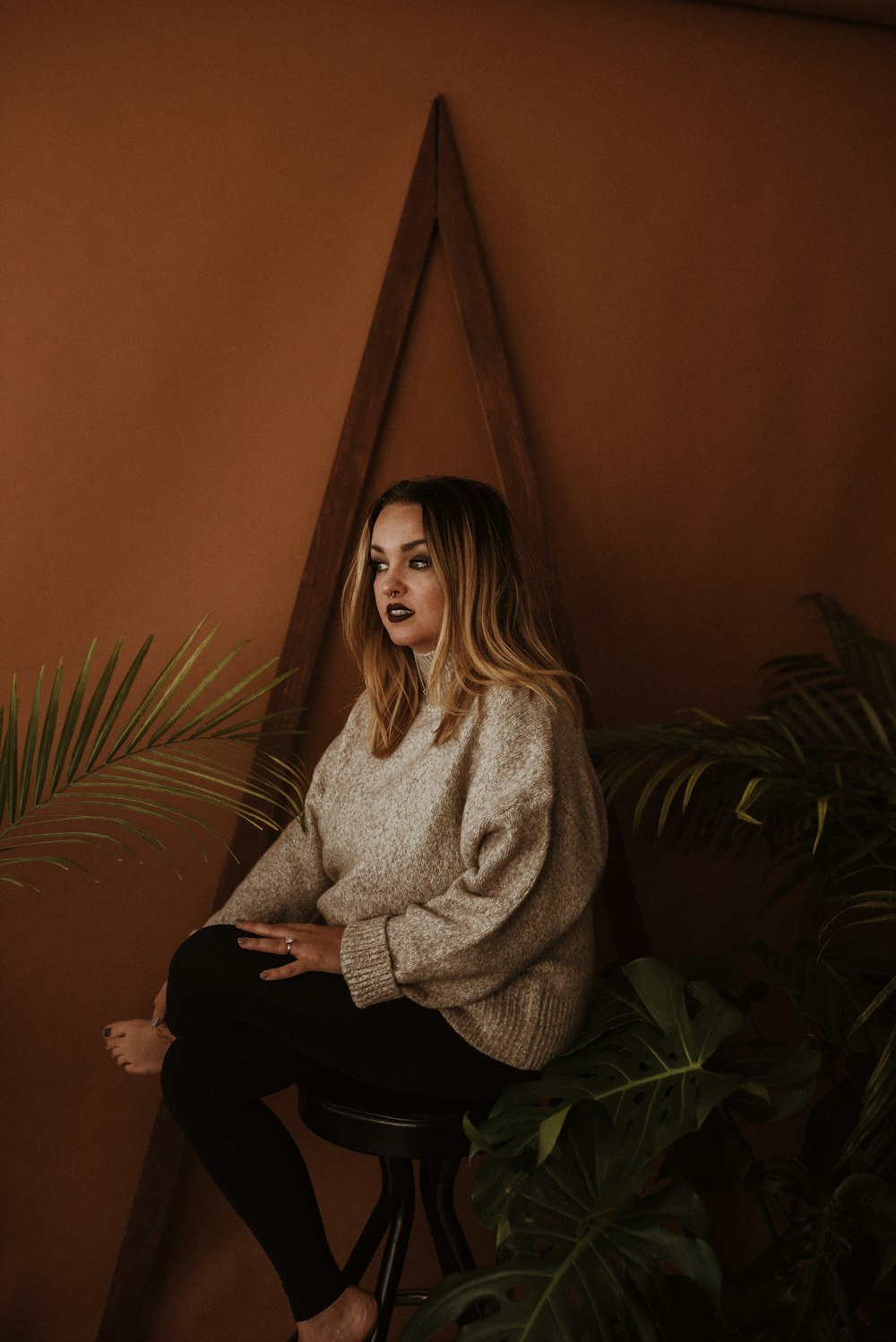 a woman sitting on a stool in front of a plant