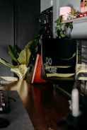 A modern workspace featuring a computer monitor with the words 'Do More.' partially visible. The desk includes a keyboard, mouse, and large leaves from a potted plant, adding a touch of nature. A shelf above holds a lamp and small red car models. The setup is sleek, combining technology and greenery.