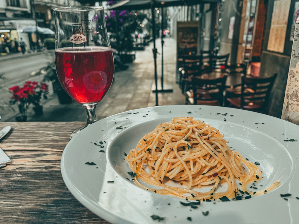 a white plate topped with spaghetti next to a glass of wine