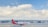 A SpiceJet airplane is positioned on the runway with a large modern terminal building in the background. The sky is mostly clear with a few scattered clouds. The airplane is white with a red tail that features a yellow design.
