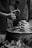 Hands are actively shaping clay on a pottery wheel, demonstrating the art of pottery-making. Two sets of hands are visible, one guiding and the other learning. The scene is intimate and focused, showcasing a transfer of skills.