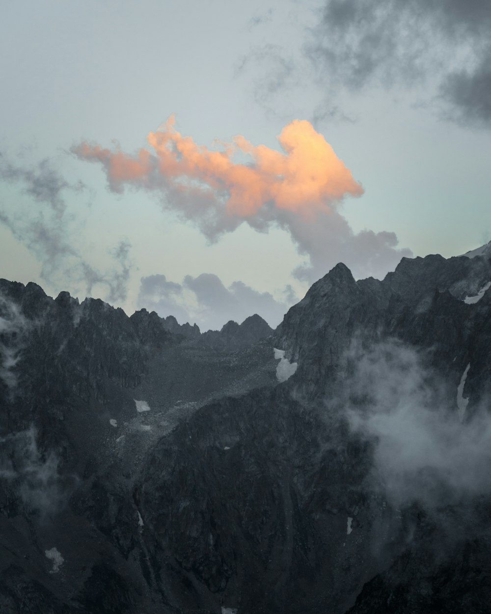 a mountain range with clouds and a pink cloud in the sky