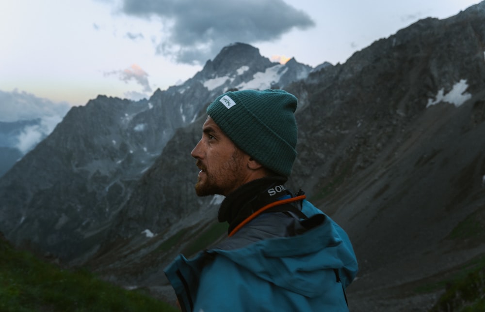 a man wearing a green hat standing in front of a mountain