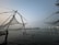 Large fishing nets are suspended over the water using wooden structures at dusk. The horizon is visible in the distance, with lights from a distant shoreline reflecting off the calm water surface.