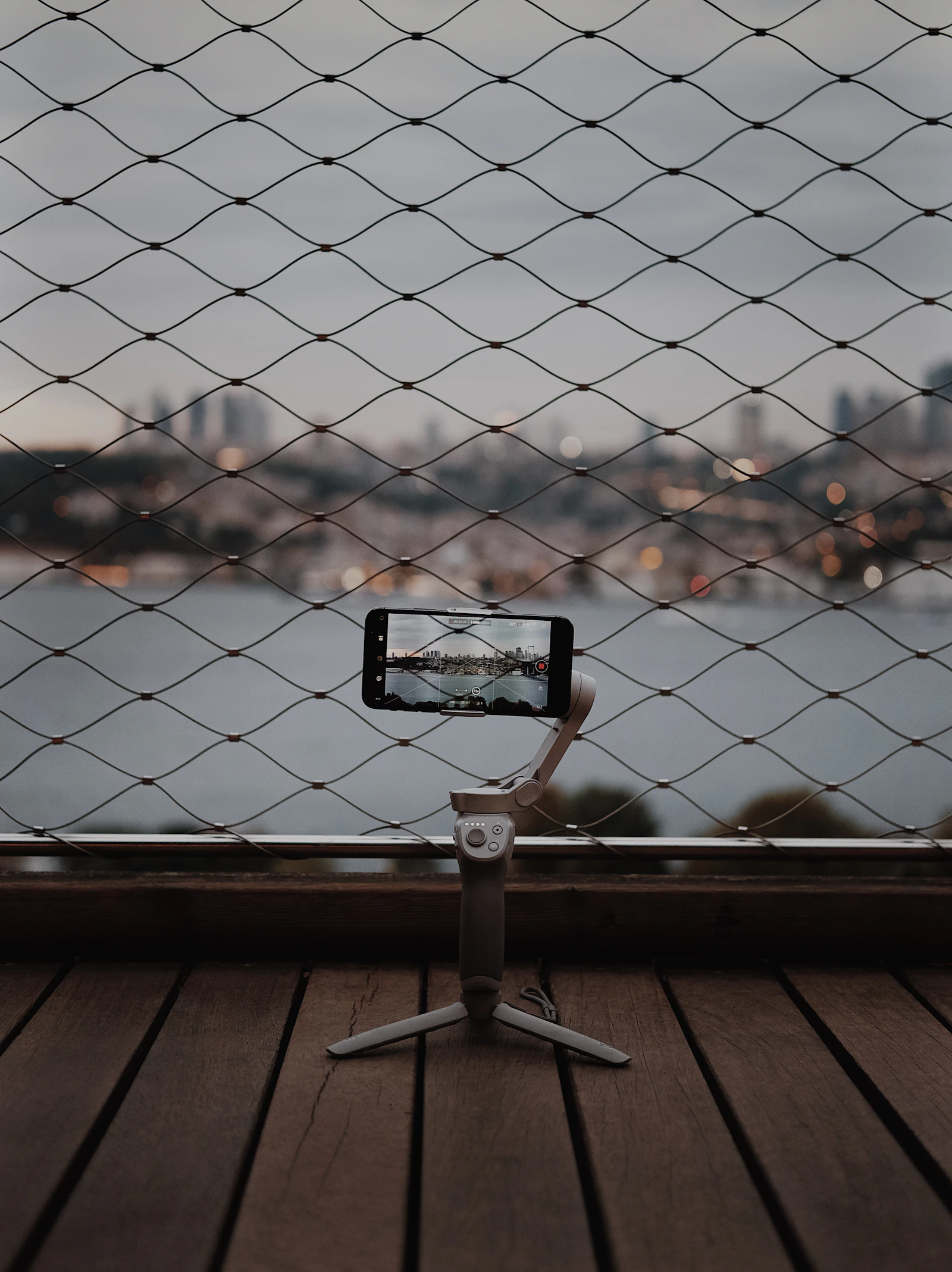 A smartphone on a gimbal filming a city skyline across the water at dusk
