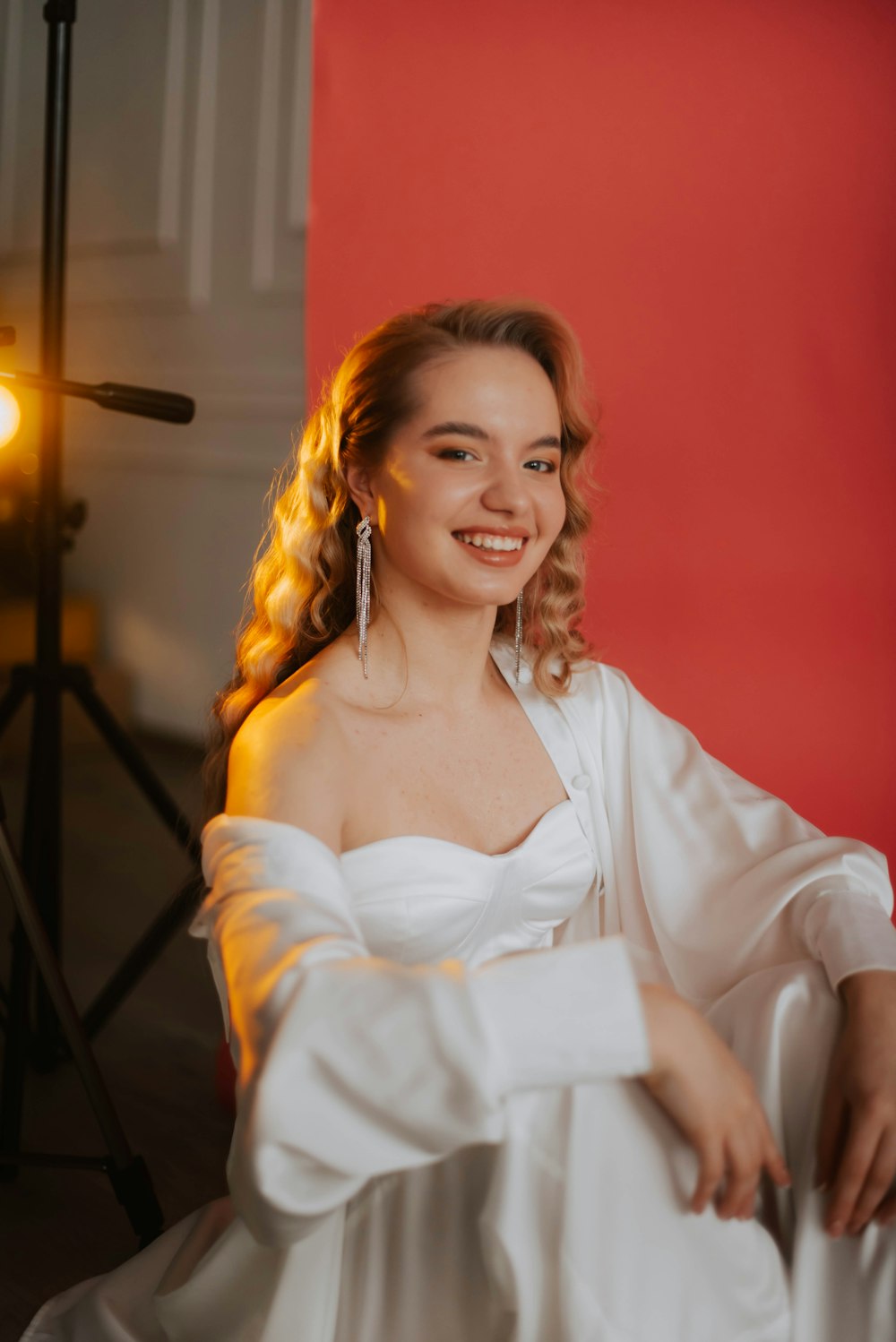 a woman in a white dress sitting in front of a red wall