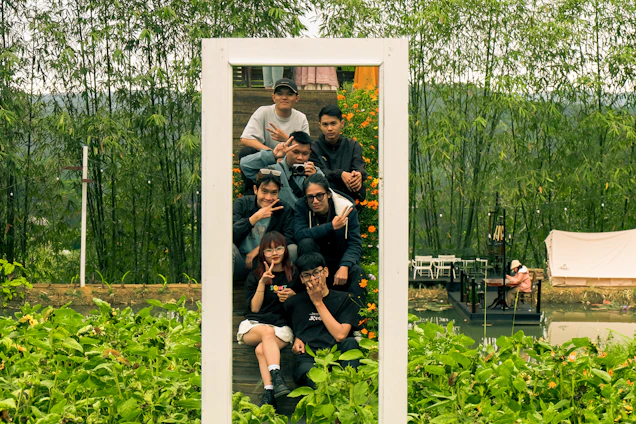 A group of young people collaborating outdoors surrounded by lush greenery and sunlight.