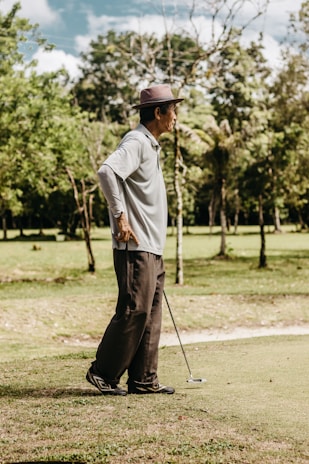 An older man smiling warmly while holding a golf club on a sunny course.