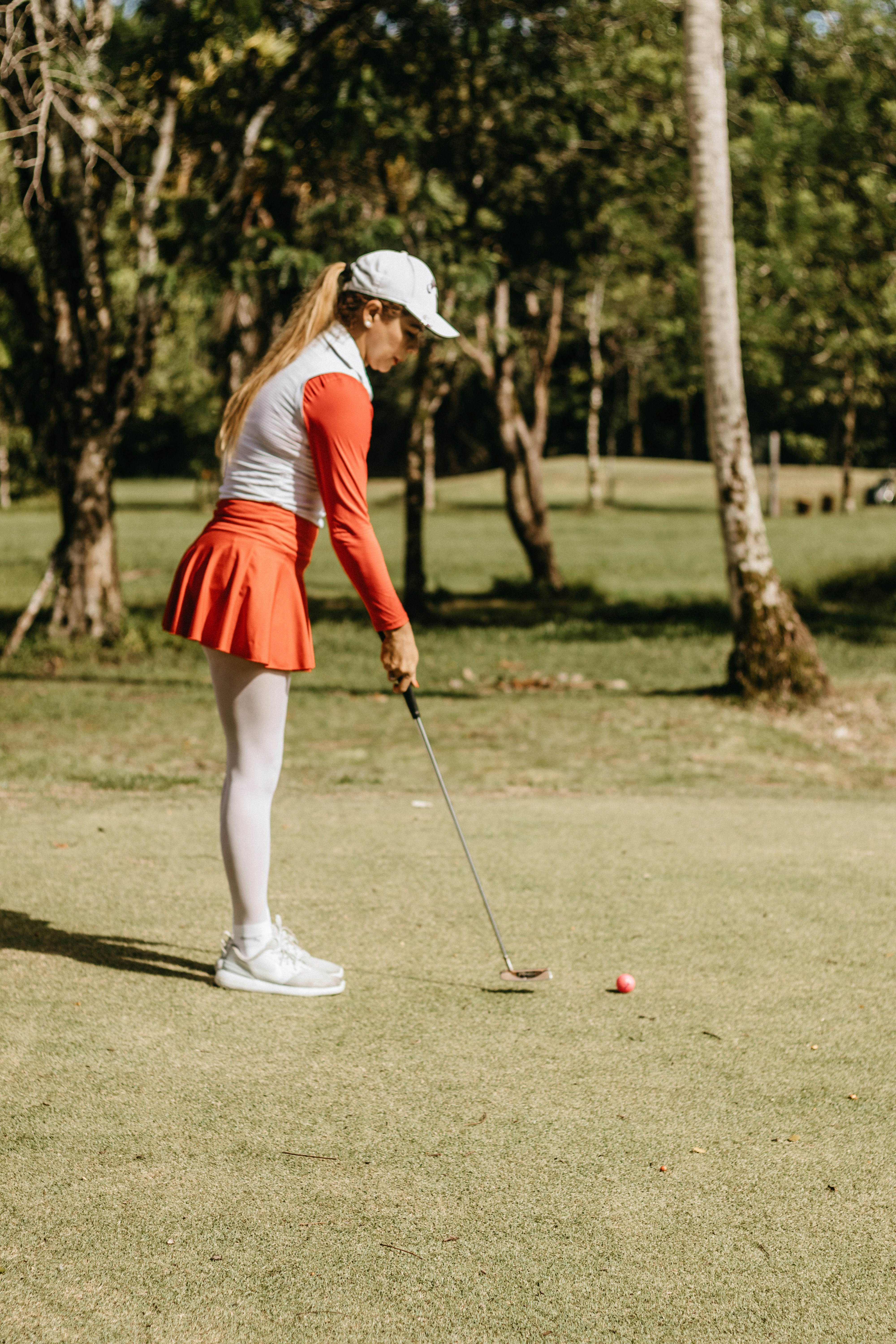A woman golfer in a soft green sweater lining up a putt on a sunlit, manicured green.