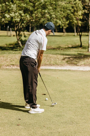 Athlete practicing putting with iniputter under bright natural light on a golf course.