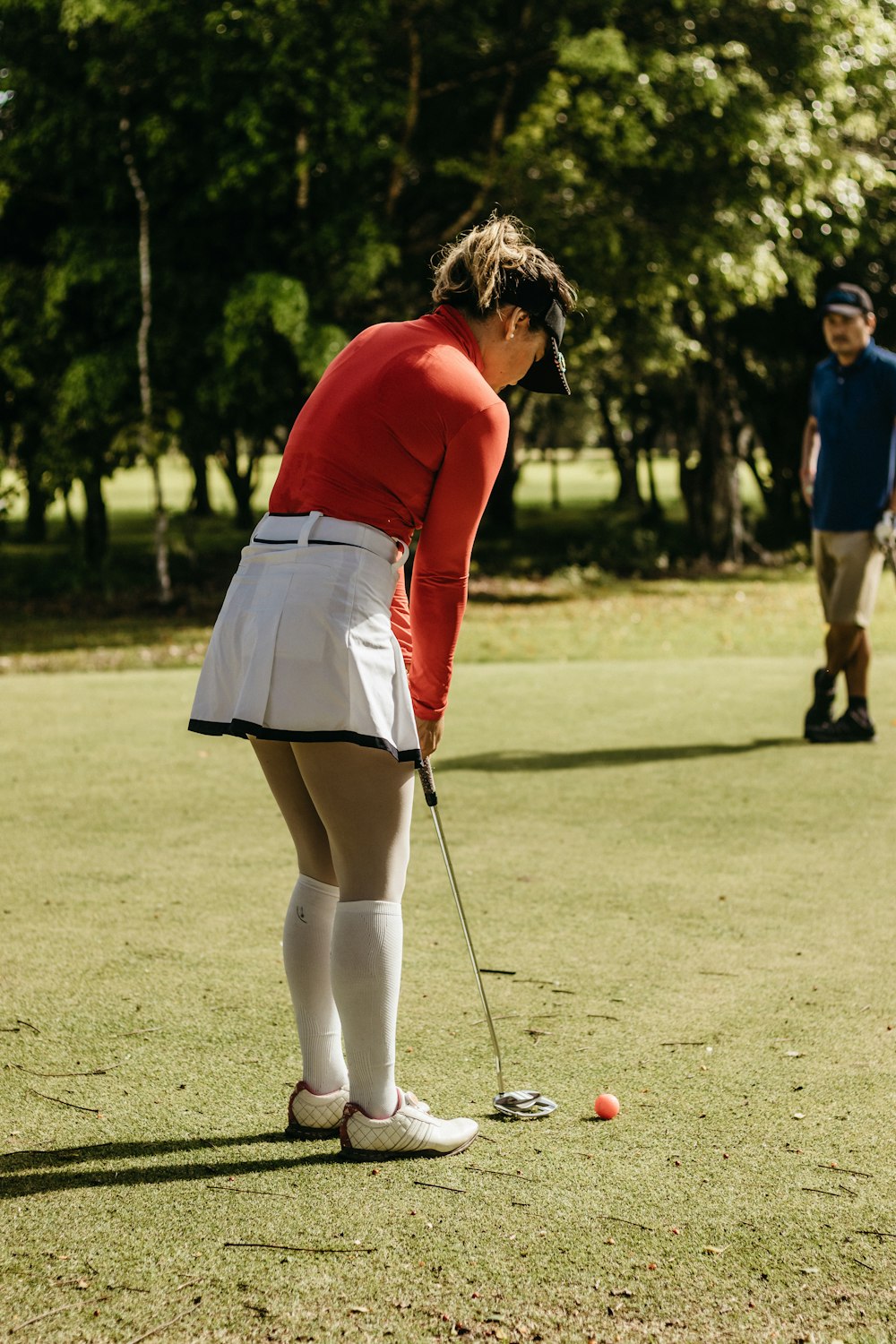 a woman in a red shirt and white skirt playing a game of golf