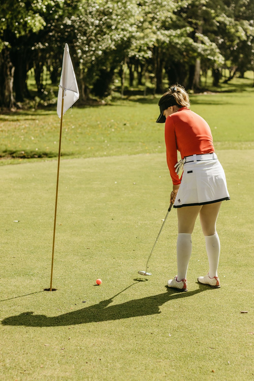 a woman in a red shirt and white skirt playing golf