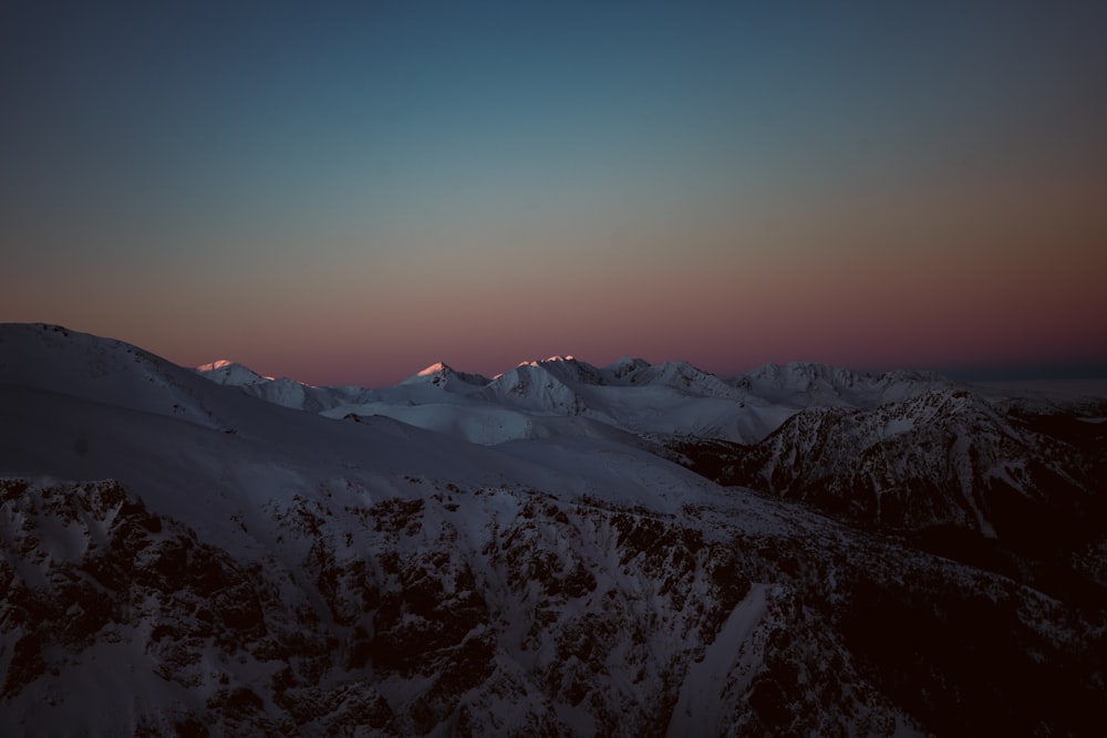 a view of a snowy mountain range at dusk