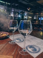 A dimly lit hotel bar corner with two half-full wine glasses and a flickering candle casting shadows.