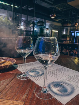 Elegant wine glasses filled with red and white wine set against a cozy, dimly lit restaurant background.