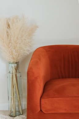 A cozy living room corner featuring a tall, slender vase holding fresh green branches beside a comfy armchair.