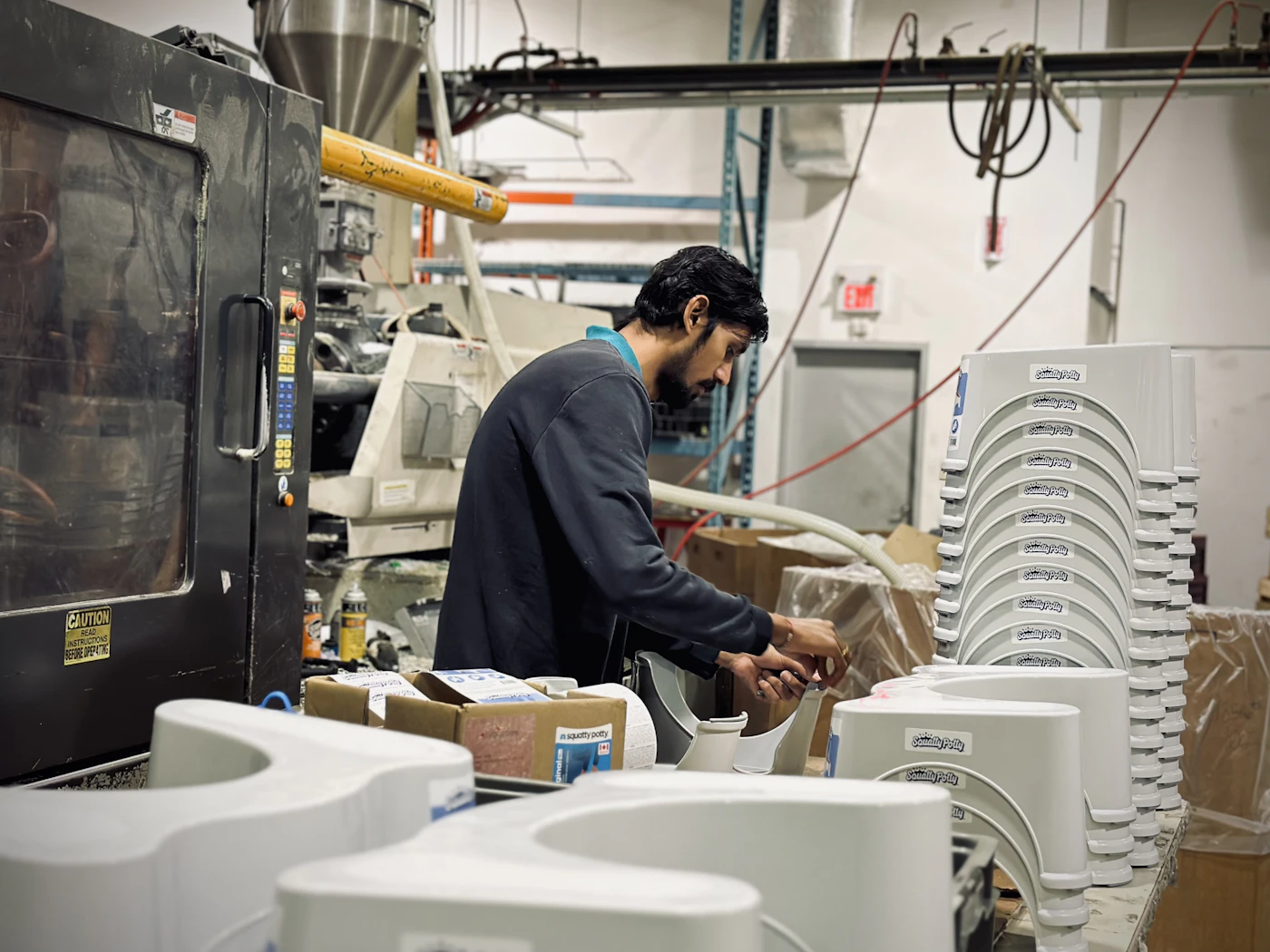 A technician working at an injection molding machine beside stacks of freshly molded plastic parts