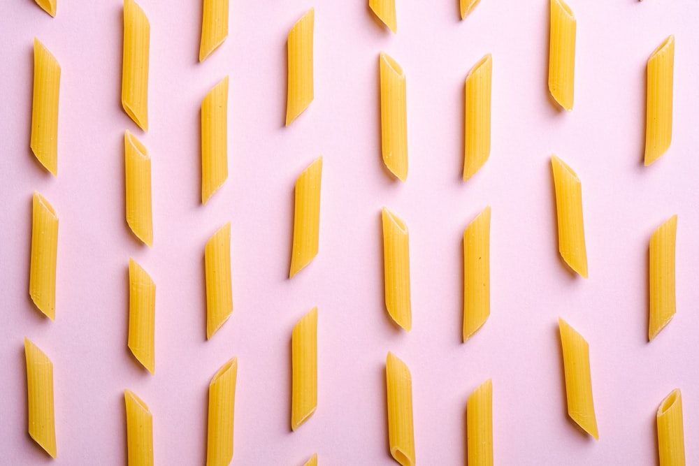 a pink background with yellow pieces of pasta