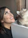 A happy woman reading pet care tips on a laptop with her cat beside her.