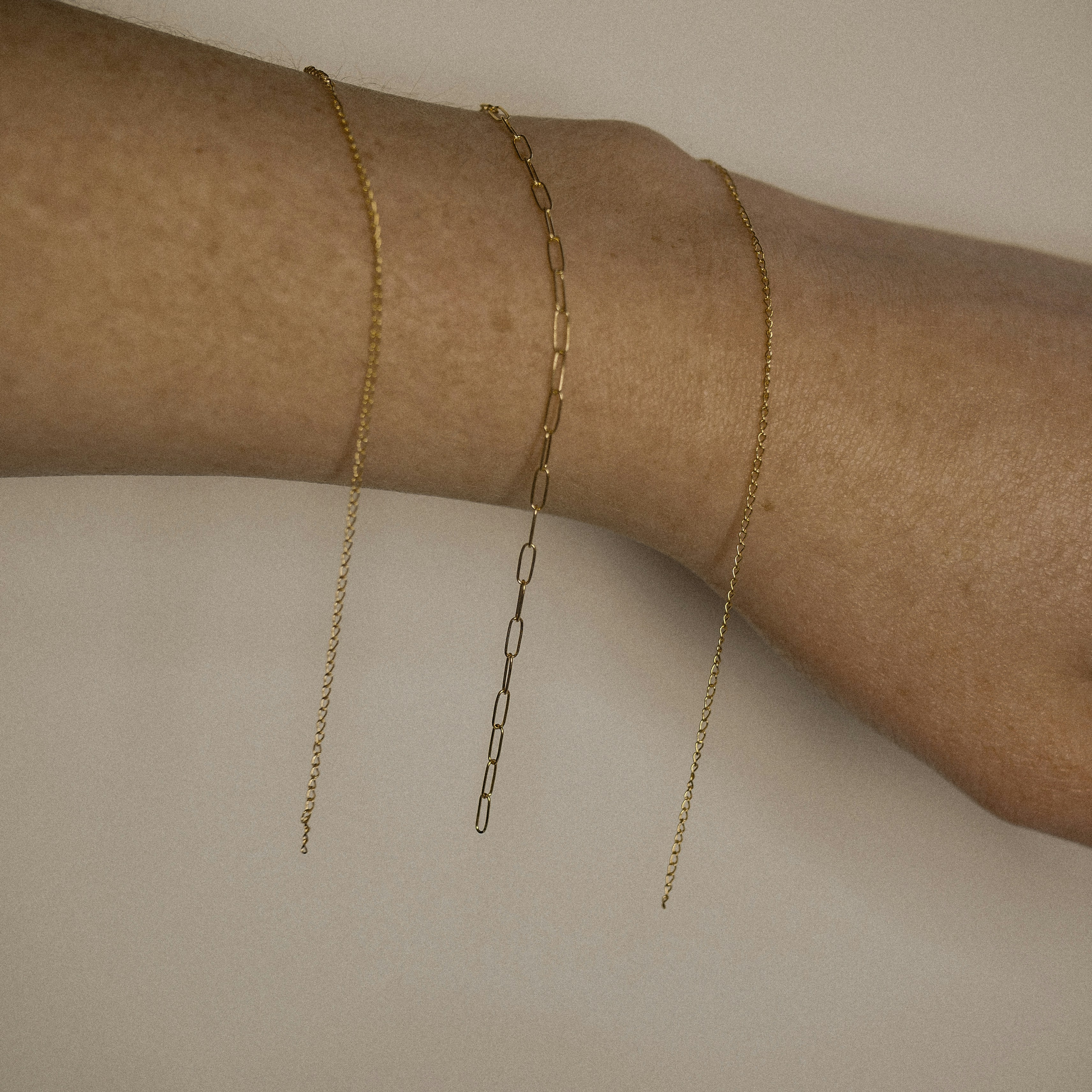 a woman's arm with three gold chain bracelets on it