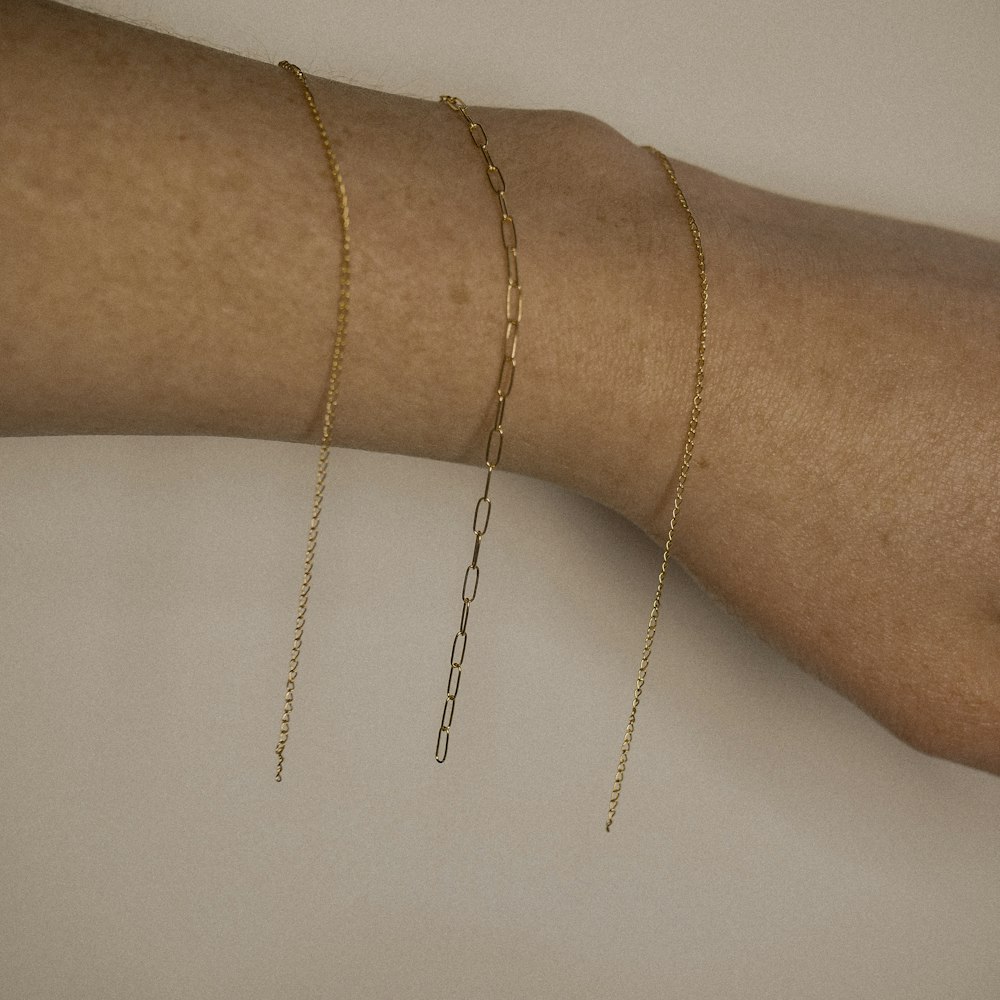 a woman's arm with three gold chain bracelets on it
