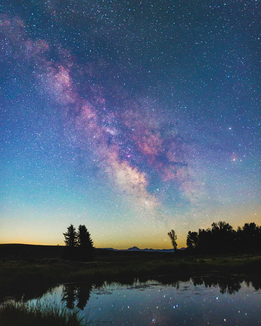 the night sky is filled with stars and the milky is reflected in the water