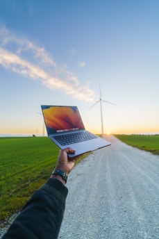 Engineer analyzing data charts on a laptop in front of a wind farm at sunset.