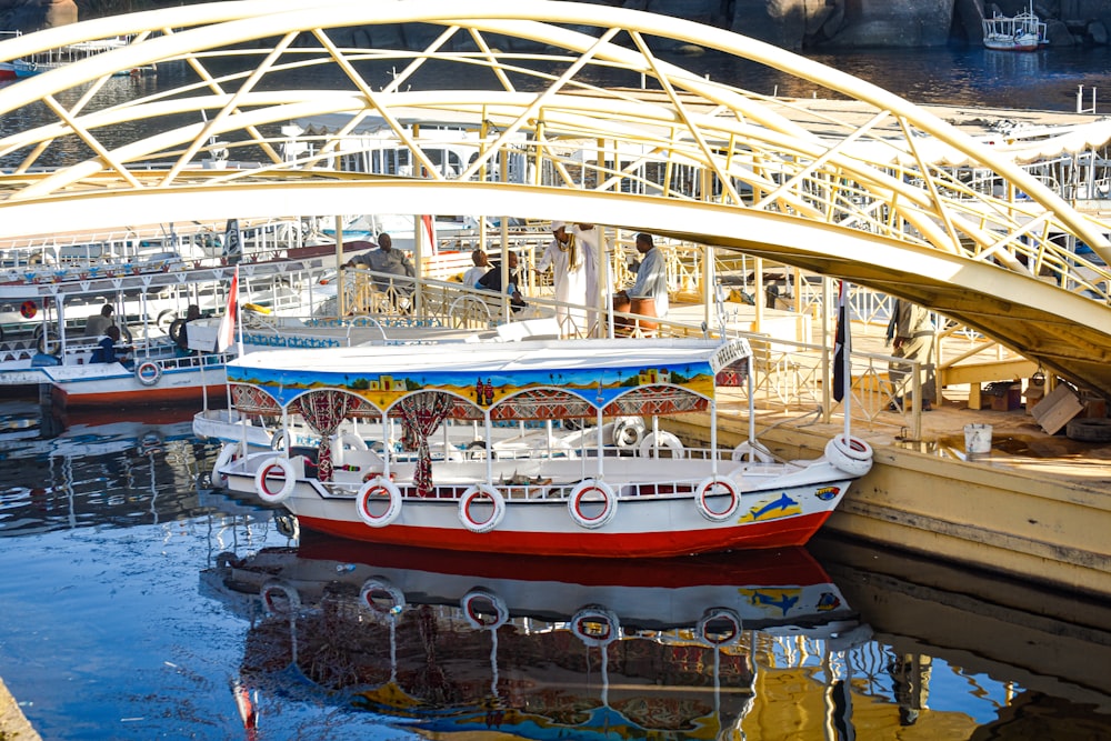 a red and white boat sitting in the water under a bridge