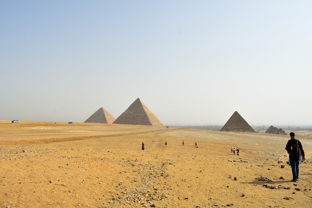 Un hombre parado frente a tres pirámides en el desierto