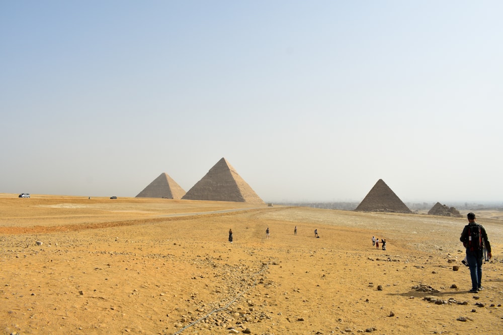 a man standing in front of three pyramids in the desert