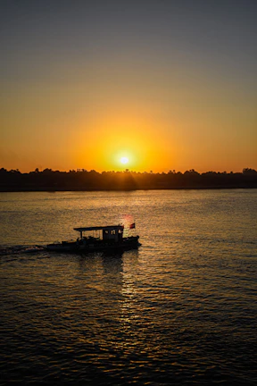 A serene sunset over the Sundarbans mangrove forest, with a boat gently gliding through the water.
