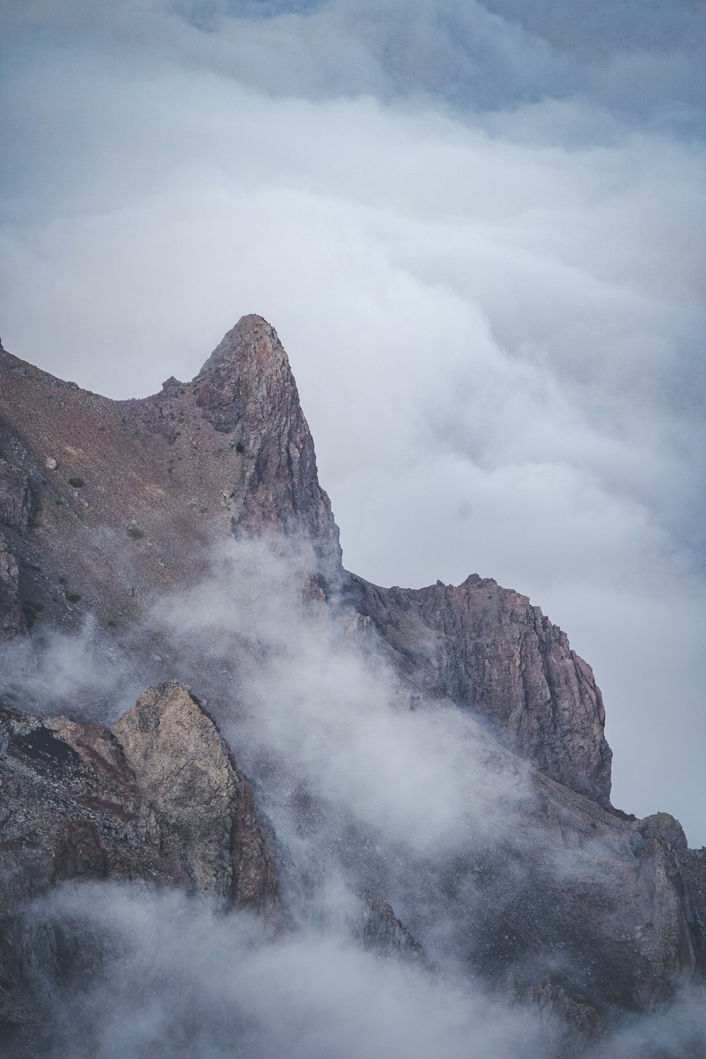 a very tall mountain surrounded by clouds in the sky