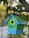Close-up of a colorful handcrafted birdhouse hanging on a tree branch in a sunny garden.