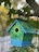 Close-up of a colorful handcrafted birdhouse hanging on a tree branch in a sunny garden.