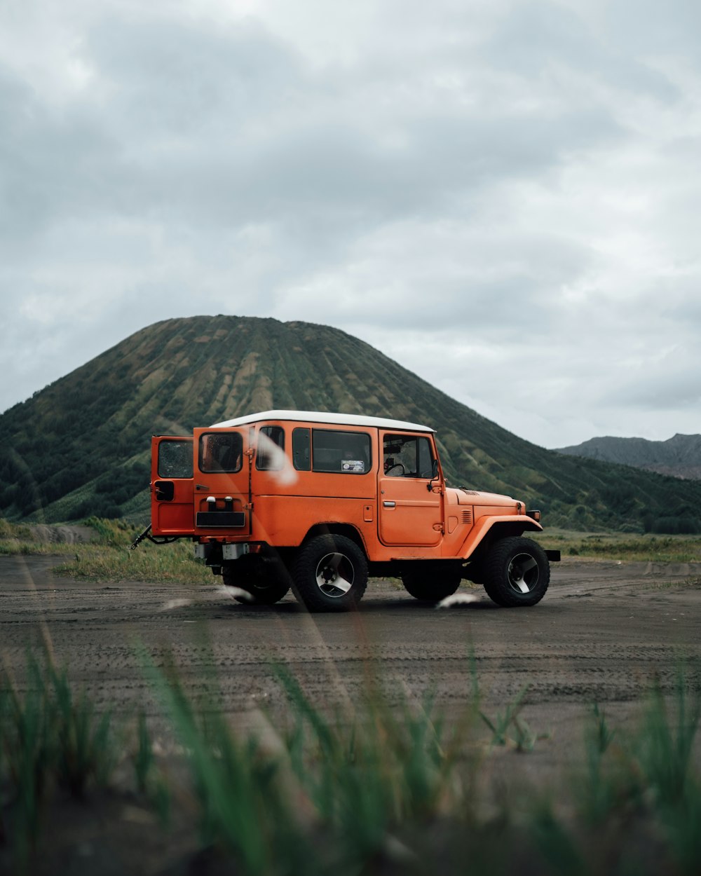 an orange jeep is parked in front of a mountain