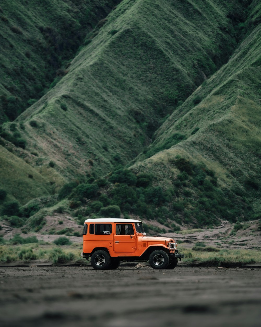 an orange jeep is parked in front of a mountain