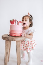 a little girl sitting in front of a pink cake