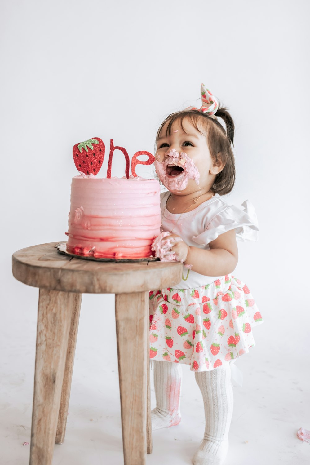 a little girl sitting in front of a pink cake
