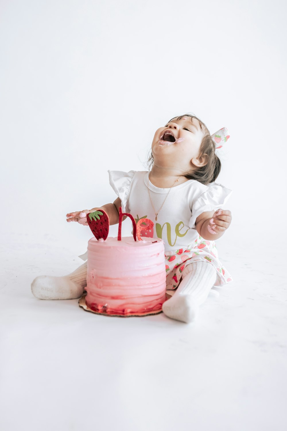 a little girl sitting in front of a pink cake