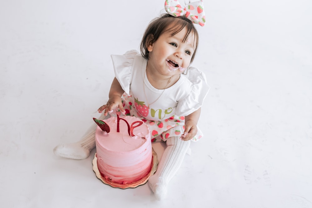 a little girl sitting in front of a pink cake