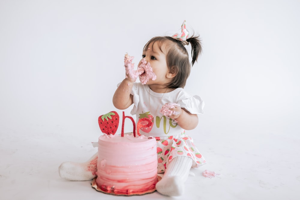 a little girl sitting in front of a pink cake