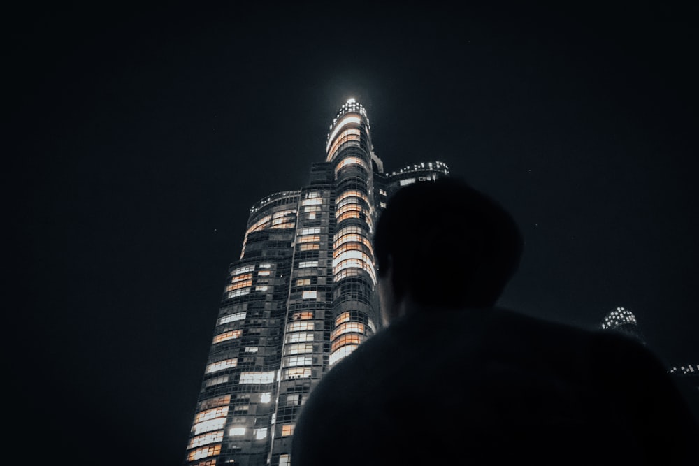 a man standing in front of a tall building at night