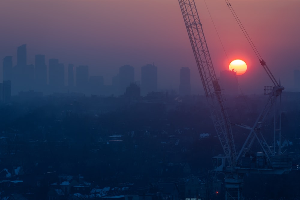 the sun is setting behind a crane in a city
