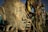 A collection of abstract sculptures made of metal and other materials, resembling human figures and faces. The weathered, textured surface of the large head in the foreground suggests uniqueness and creativity.