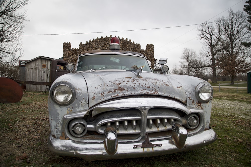 an old car parked in a field with a house in the background