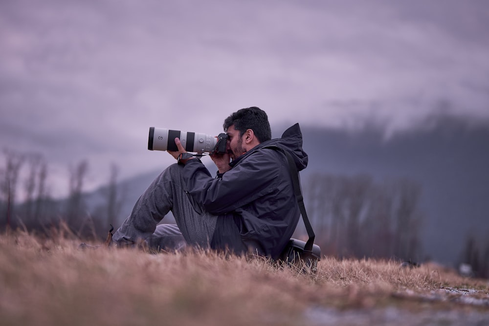 a man sitting in a field taking a picture with a camera