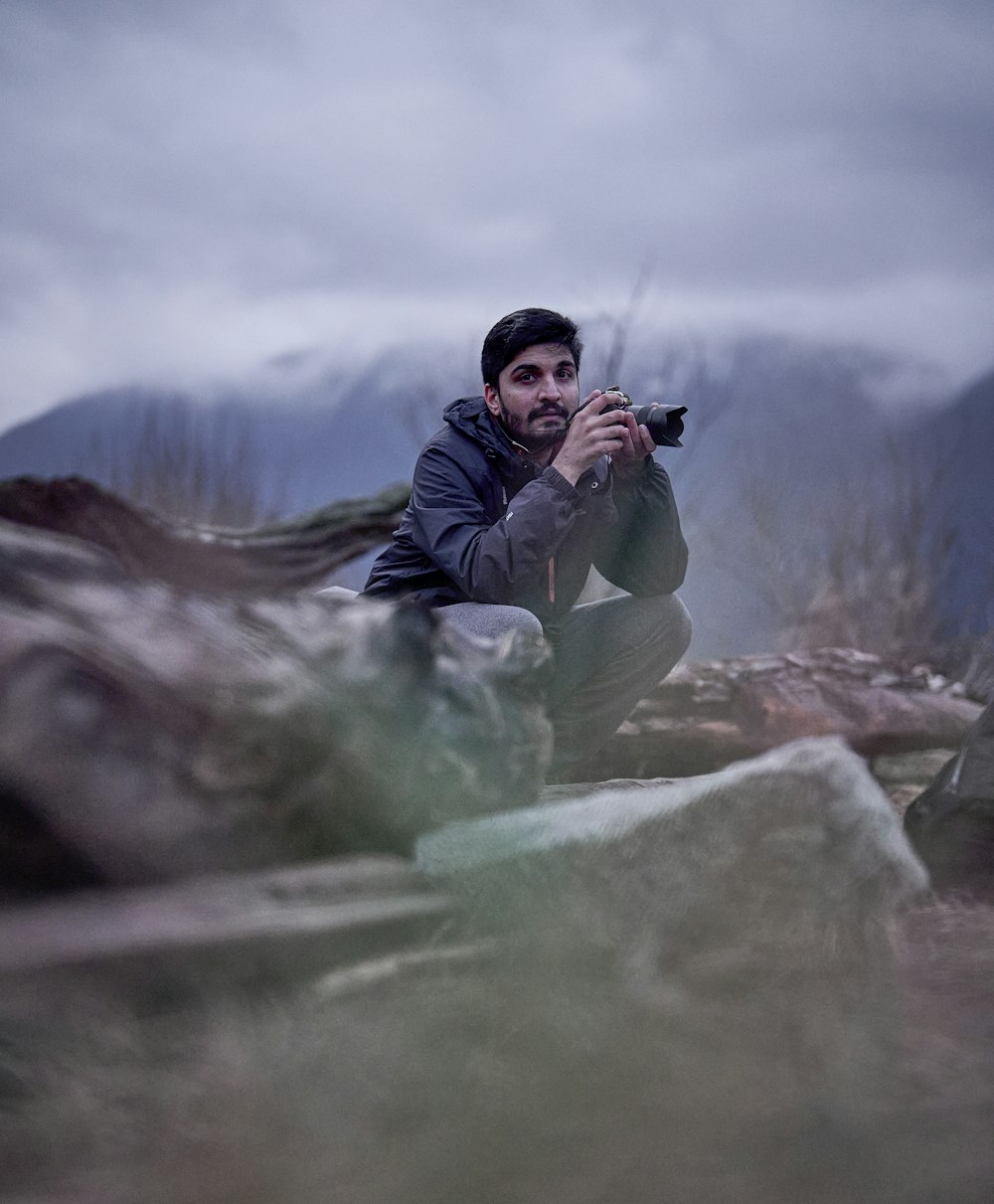 a man sitting on top of a pile of rocks holding a camera