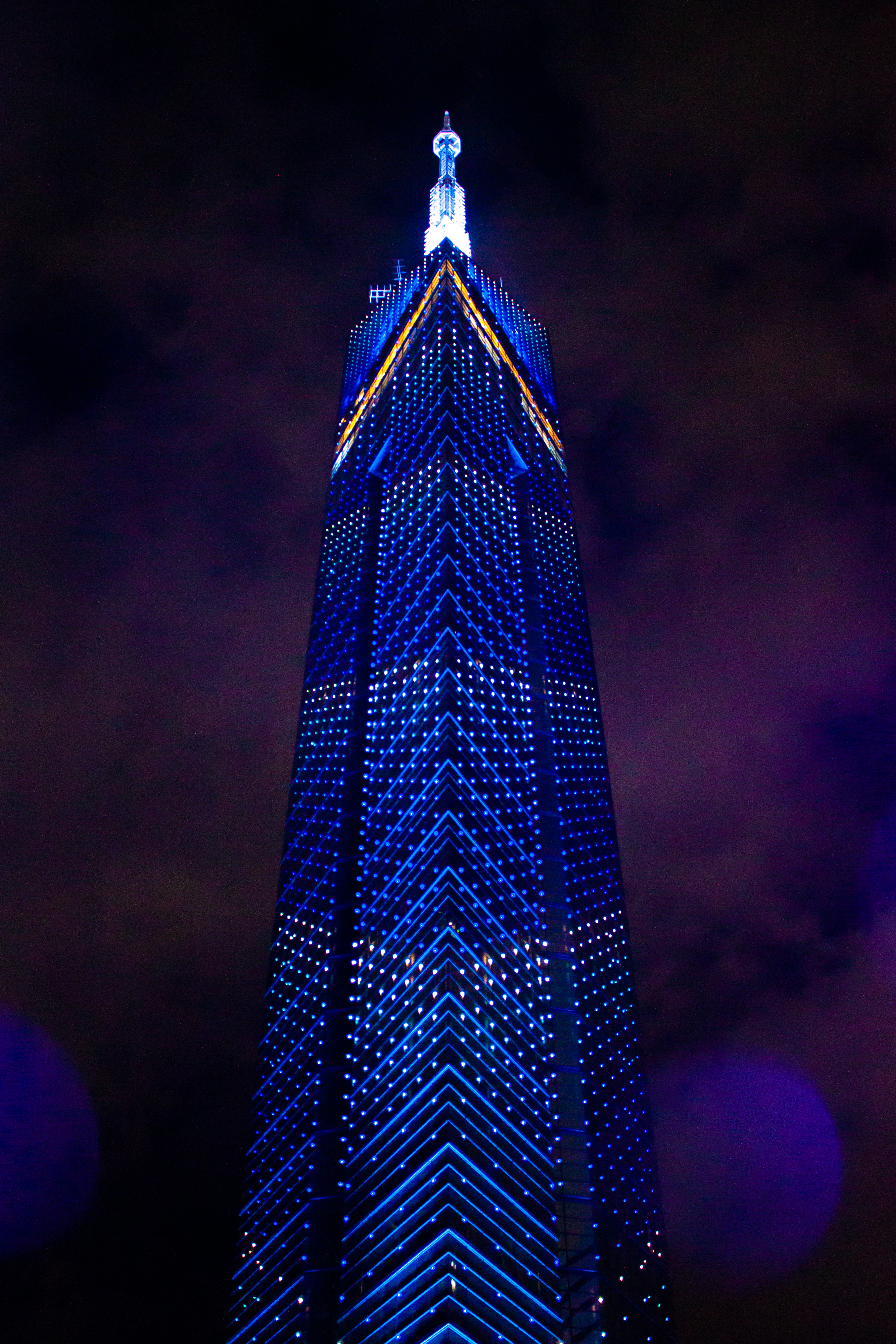 Fukuoka Tower rising into the night above the Momochi waterfront, its mirrored flanks covered in a grid of blue and white lights running up to the lit spire at the top.